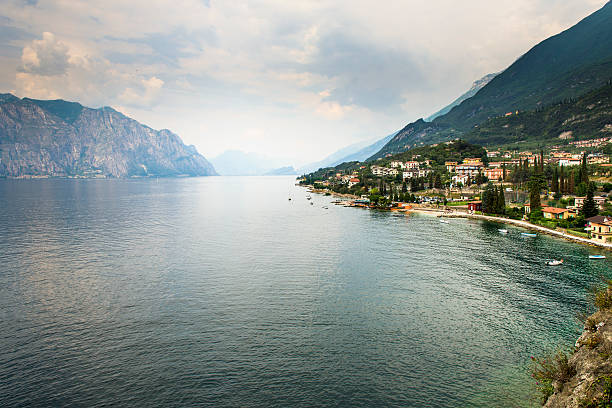 In the distance, a sailing yacht sails along the sea bay against the background of mountains and a blue sky. In the foreground is a stone pier. Picturesque seascape