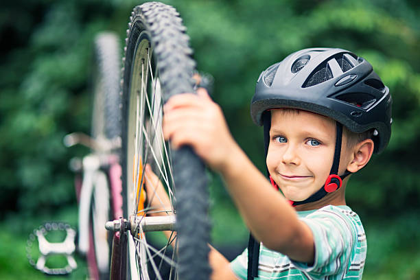 Smiling little boy aged 6 repairing a bicycle. The boy is wearing a bicycle helmet.