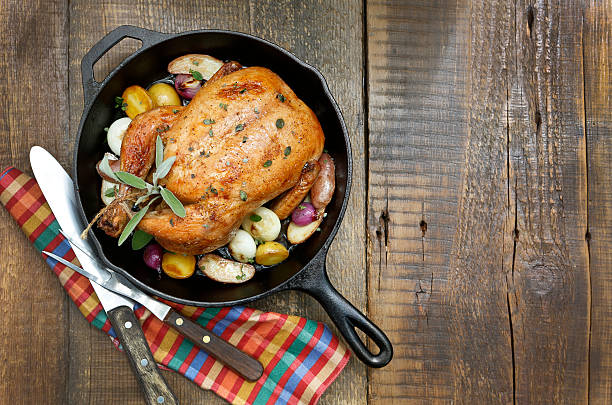 Roast Chicken with Potatoes and Onions in Cast Iron Pan. A overhead view of a roast chicken on a rustic wood table top. cooking pan photos stock pictures, royalty-free photos & images