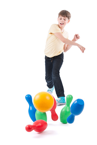 Boy knocking down the pins by throwing a bowling ball. Isolated on white image.
