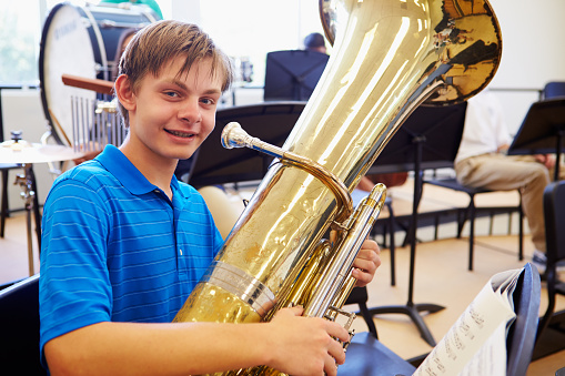 Male Pupil Playing Tuba In High School Orchestra Smiling To Camera