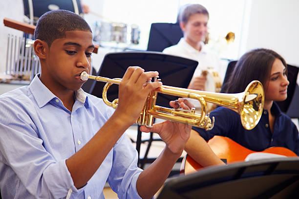 male pupil playing trumpet in high school orchestra - trompet stockfoto's en -beelden