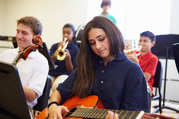 istock Female Pupil Playing Guitar In High School Orchestra 498130135