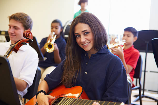 istock Female Pupil Playing Guitar In High School Orchestra 498130147