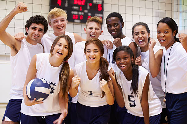 Portrait Of High School Volleyball Team Members With Coach Portrait Of High School Volleyball Team Members With Coach Holding Ball Smiling To Camera sports uniform photos stock pictures, royalty-free photos & images