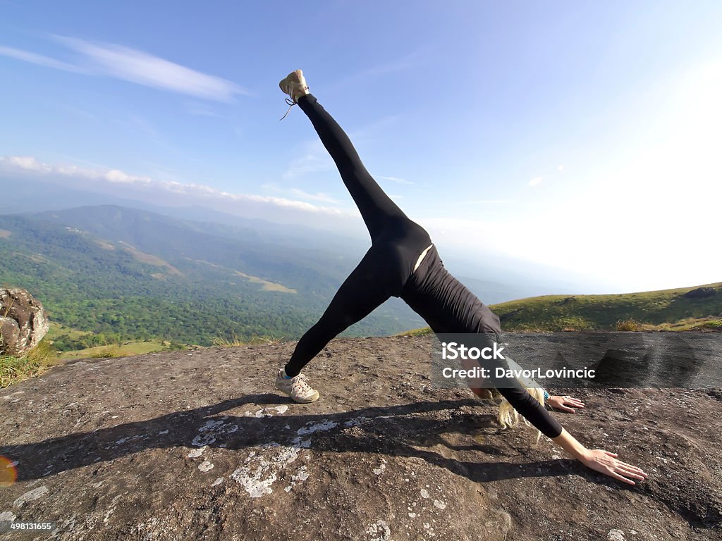 Top of mountain Young Woman stretching her leg on the top of mounting above Munnar Tea fields on around 1600 m above sea level in the Western Ghats range of mountains in the southwestern state of Kerala, India. It is part of UNESCO World Heritage Site as one of the eight hottest places of biological diversity in the world. Adult Stock Photo