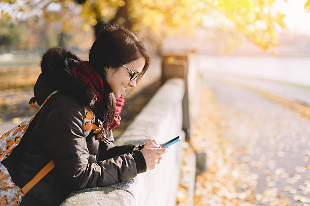 istock Girl in the autumn park text messaging 498143316