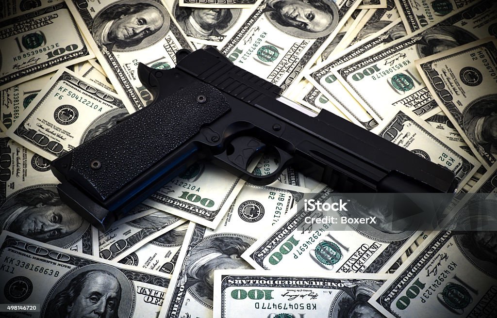 Black and chrome gun pistol and money dollars background Black and chrome gun pistol and money dollars background high contrasted with vignetting effect Currency Stock Photo