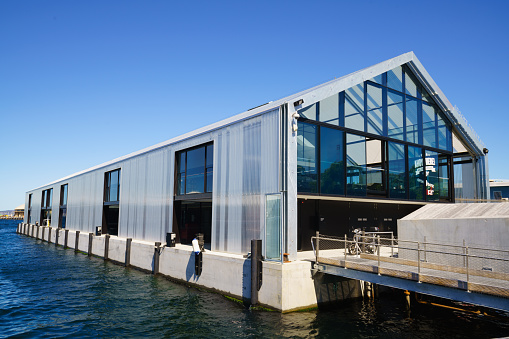 Hobart, Tasmania, Australia - November 4, 2015: Waterfront promenade view to the Brooke Street Pier in the Harbor of Hobart, Tasmania. Modern Architecture Ferry Terminal Building to the ferry MR-I MONA ROMA towards the famous MONA (Museum of Old and New Art) Museum in Hobart under a blue sunny cloudless sky. 