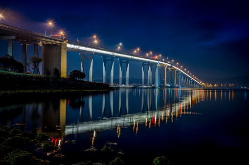 Famous Tasman Bridge (Total Length: 1,396 metres (4,576 ft) ) crossing the Derwent River towards the City of Hobart at night. The illuminated bridge, on of the major icons - symbols of Hobart - mirroring in the calm Derwent River Water, Hobart, Tasmania, Australia.
