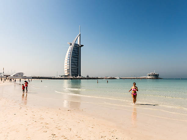 Dubai, United Arab Emirates - January 25, 2014: Tourists on Jumeirah Beach and luxury Burj al Arab hotel in background