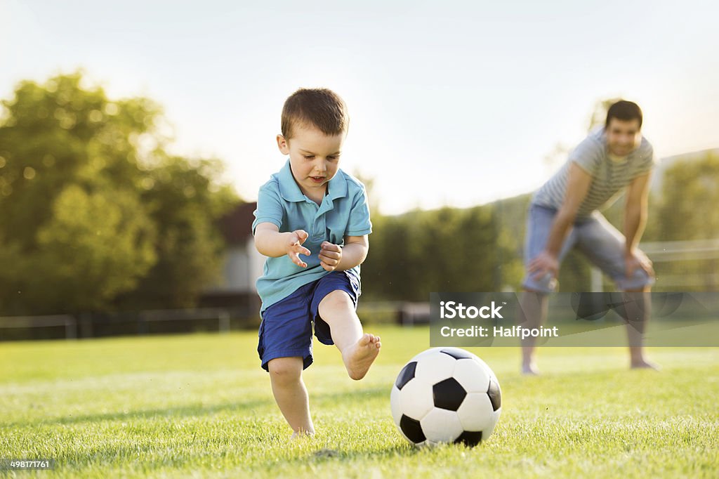 Father and son playing football Young father with his little son playing football on football pitch Soccer Stock Photo