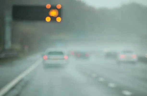 The M6 motorway in England on a wet November day, with speed warning lights flashing overhead. Defocused to highlight poor visibility.