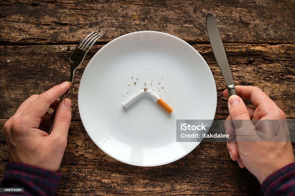 man holding a knife and fork next plate with cigarette man holding a knife and fork next to a white plate with a cigarette 2015 Stock Photo