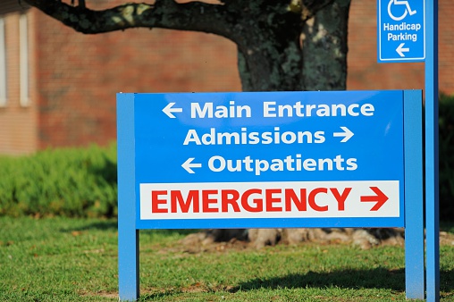 Close up photograph of main entrance admissions outpatients emergency directional sign in front of hospital.