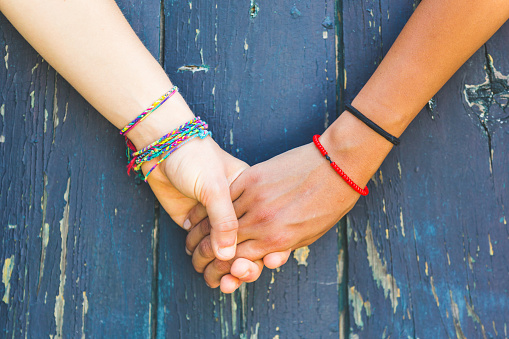 Two women holding hands with a wooden background. One is caucasian, the other is black. Multicultural, homosexual love and friendship concepts.