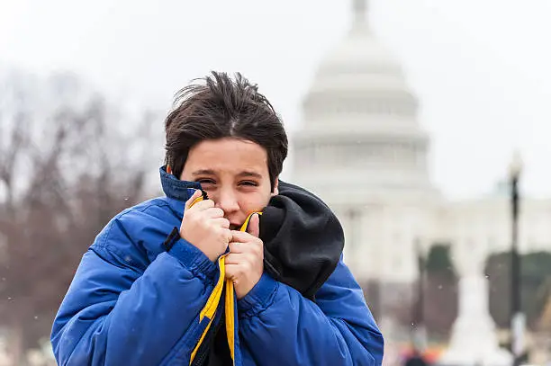 Child feeling very cold in a winter windy and snowing cold day with the Washington dc capitol in the background
