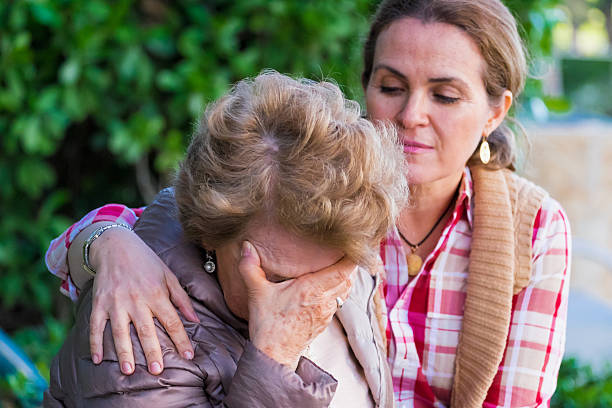 Crying senior woman holding her face being comforted Senior woman with her hands on her head looking down sitting in a park bench with her daughter consoling her senior adult women park bench 70s stock pictures, royalty-free photos & images