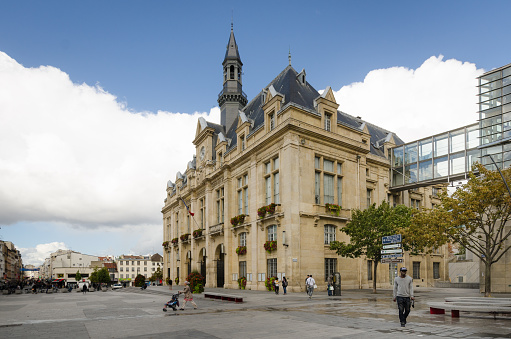 Saint-Denis, France - September 14, 2015: People are walking in front of the City Hall which overlooks Place Victor Hugo with Rue de la Republique in the distance. Saint-Denis is a suburb of the French capital, Paris.