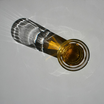 Bird's eye view of whiskey glass and its shadow on a white table