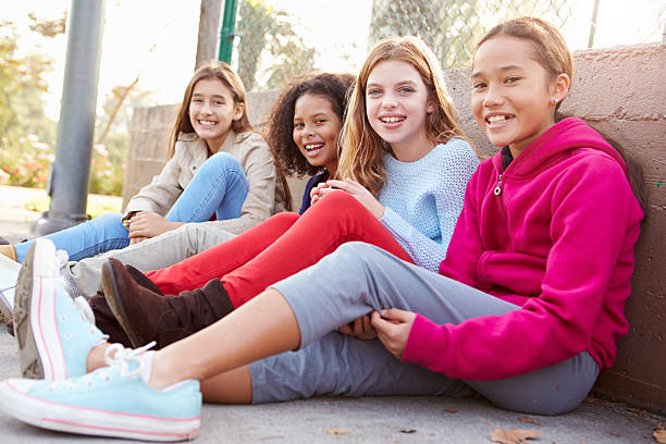 four young girls hanging out together in park - meisjes stockfoto's en -beelden