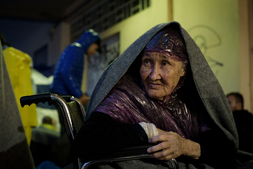 Mytlilene, Lesbos, Greece - October 23, 2015: An old woman from Mazar-i-Sharif, Afghanistan, sits in a wheelchair at the port of Mytilene, waiting for a 1:00 a.m. ferry to Athens. Accompanied by her grandkids and others, she rode a horse to the Iranian border, bused across Iran and Turkey, and on the morning this photo was taken took a crowded boat from Turkey to Lesbos during a thunderstorm. 