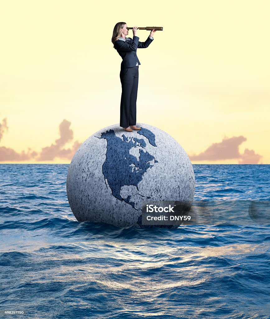 Businesswoman Looking Through Spyglass Standing On A Globe A businesswoman peers through a spyglass while standing on a globe that is adrift in the ocean.  Climate Change Stock Photo