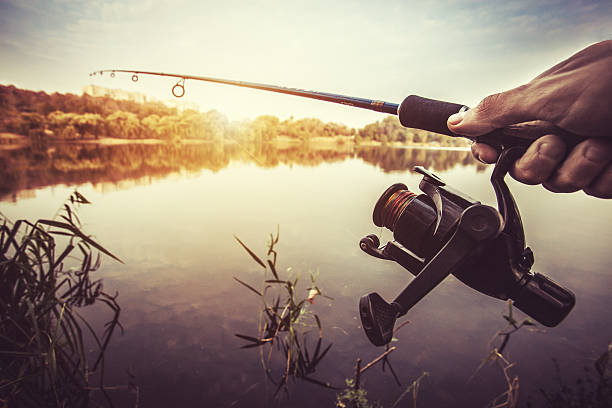 istock hand with spinning and reel on the evening summer lake 498260536