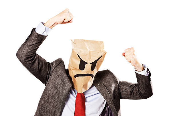 Businessman in frowning paper-bag mask shakes fists furiously A mature businessman, in formal business clothes, wearing a mask made from a paper bag, showing a fiercely frowning expression, shakes his fists aggressively, ready for a fight". punching one person shaking fist fist stock pictures, royalty-free photos & images