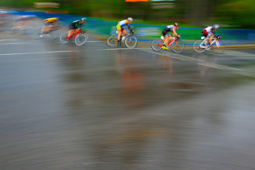 A group of male bicycle racers ride together in the rain during a criterium road bike race.
