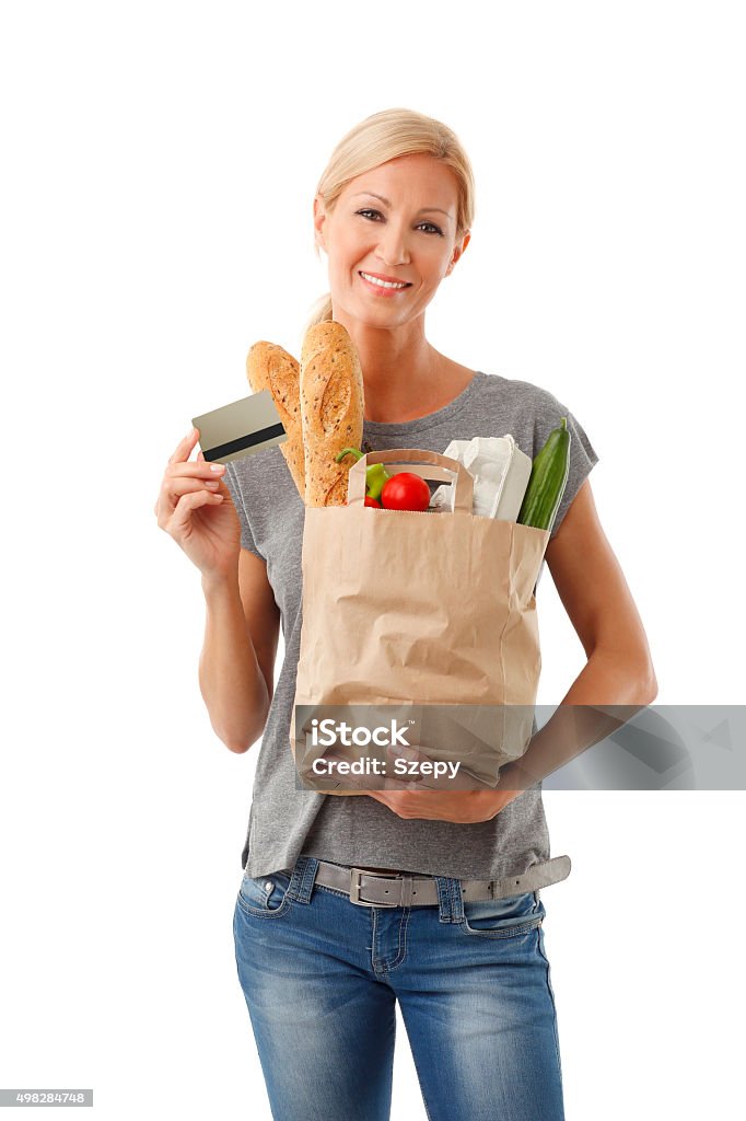 Shopping with card Portrait of smiling casual woman holding in hand a paper bag full of food and bank card while looking at camera and smiling. Isolated on white background. 2015 Stock Photo