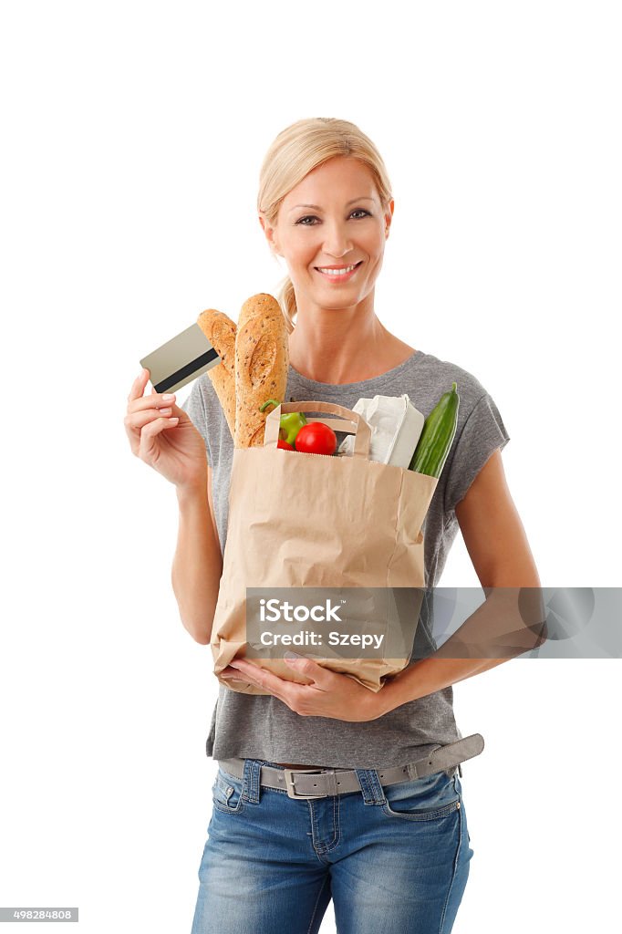 Shopping with card Portrait of smiling casual woman holding in hand a paper bag full of food and bank card while looking at camera and smiling. Isolated on white background. 2015 Stock Photo