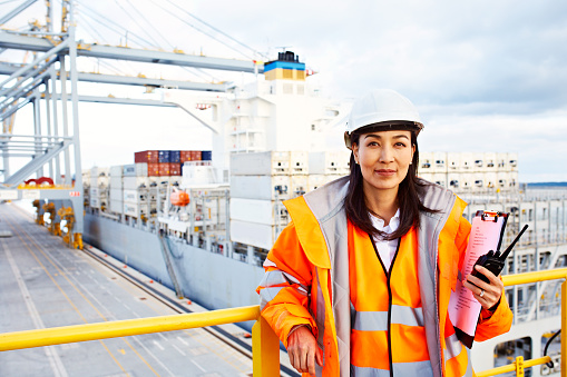 Portrait of a woman in workwear holding a walkie talkie while standing on a large commercial dock