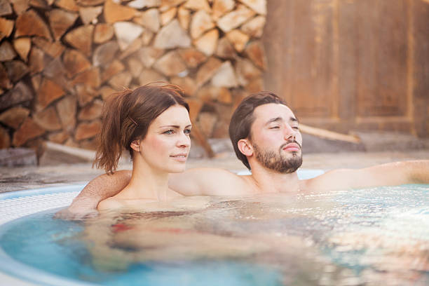 Couple enjoying in a hot tub Hot tub in wooden environment with steam in the air. Man and woman enjoying  in the water. Man embracing his woman. thermal pool stock pictures, royalty-free photos & images