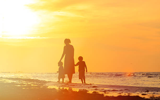istock mother and two kids walking on beach at sunset 498301016