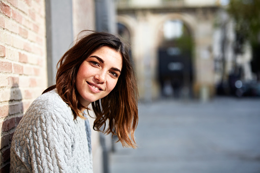 Portrait of a smiling young woman leaning against a brick wall outside