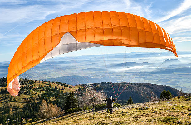 The image shows a peaceful landscape, likely Fethiye’s Ölüdeniz. A paraglider soars in the hazy sky. Below, layered green hills surround a calm body of water. The scene reflects Ölüdeniz’s serene beauty and adventurous spirit.