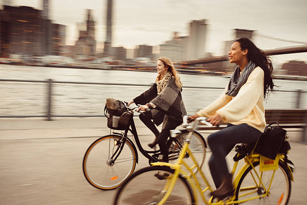 Sharing a Bicycle ride my friend in NYC Two girl friends riding their bicycles along The East River in New York City. brooklyn bridge photos stock pictures, royalty-free photos & images
