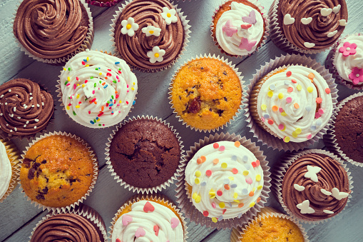 Multiple colorful nicely decorated muffins on a wooden background, top view