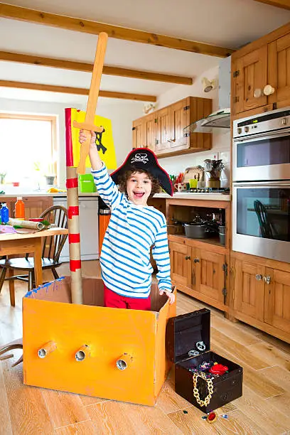 Little boy plays a role of a pirate using a cardboard box for a ship.