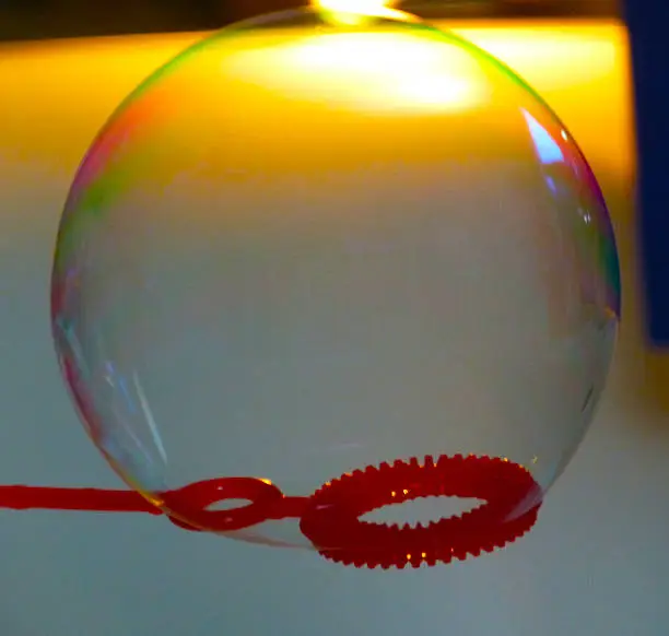 A soap-bubble with colorful reflections standing still on its bubble wand