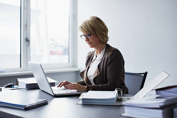 businesswoman using laptop in office - hinter stock-fotos und bilder