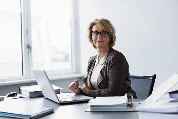 confident businesswoman sitting at desk - cheveux mi longs photos et images de collection