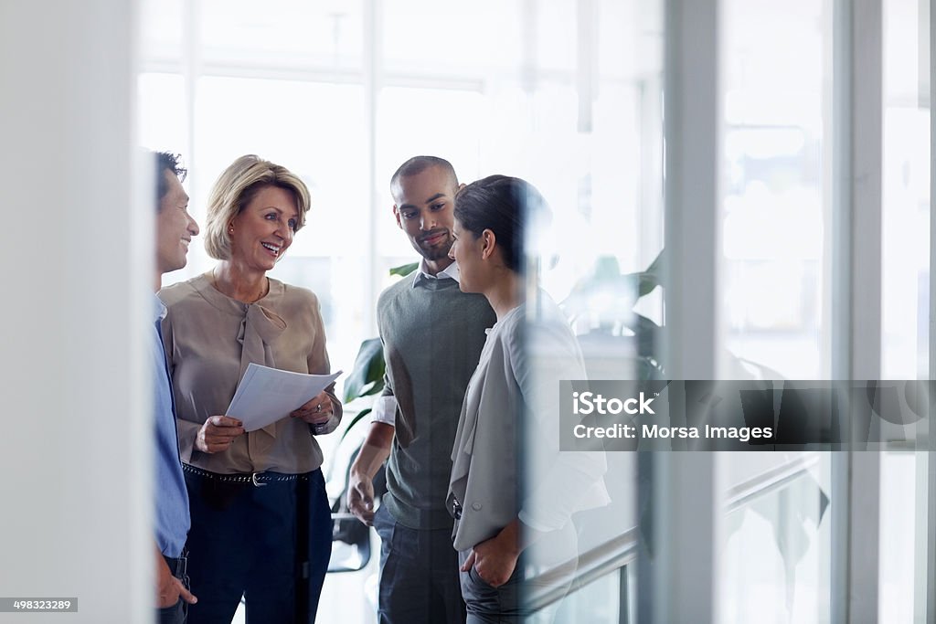 Businesswoman discussing with colleagues Smiling businesswoman discussing over document with colleagues in office Business Stock Photo