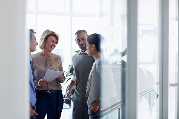 Businesswoman discussing with colleagues Smiling businesswoman discussing over document with colleagues in office business person stock pictures, royalty-free photos & images