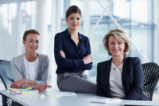 business, technology and people concept - smiling businesswoman with eyeglasses in office with team on back