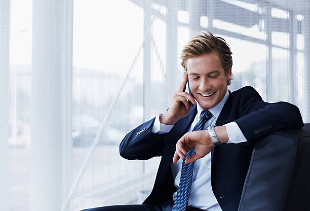 Businessman checking time in office Businessman checking time while using mobile phone in office checking the time stock pictures, royalty-free photos & images