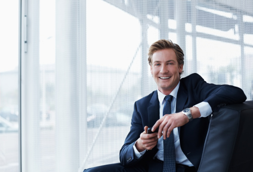 Portrait of happy businessman holding mobile phone while sitting in office
