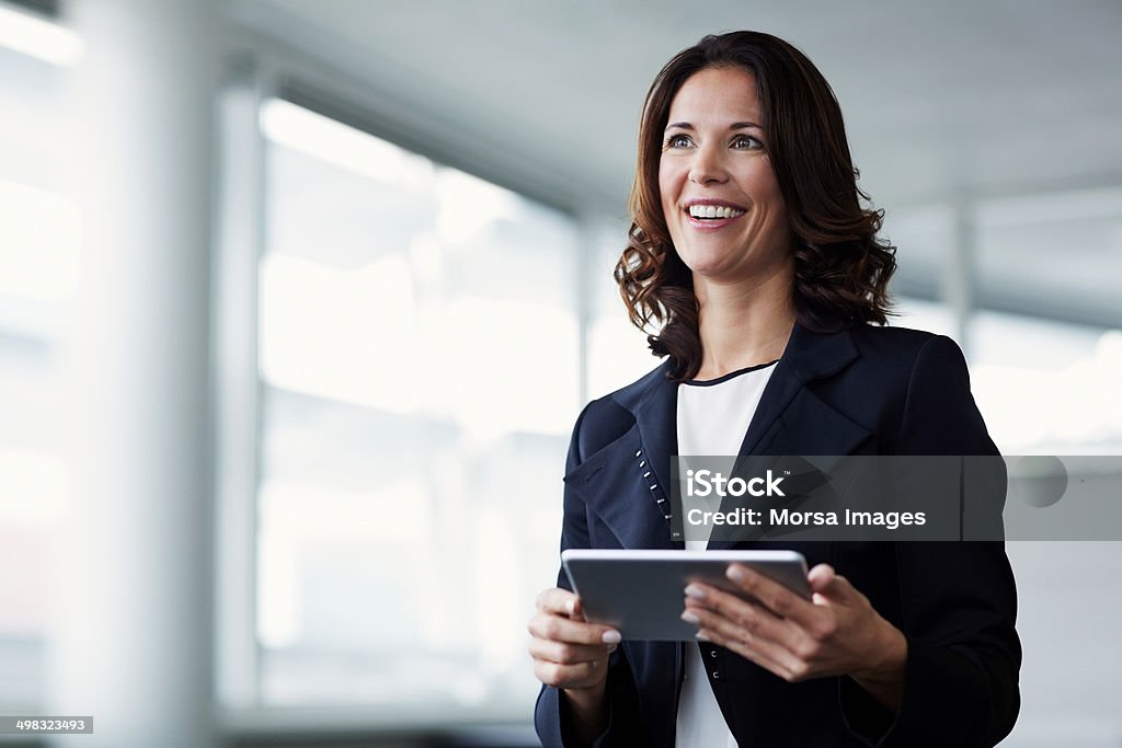 Happy businesswoman holding digital tablet Happy businesswoman looking away while holding digital tablet in office Women Stock Photo