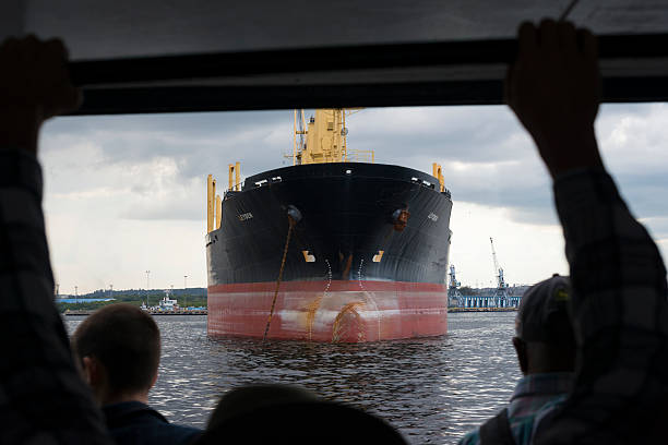 Havana, Cuba - December 16, 2014: Passengers stand in the doorway of a ferry traveling in Havana Harbor between Habana Vieja and Regla (Cuba). The ferry is passing a bulk carrier ship named Leyden.
